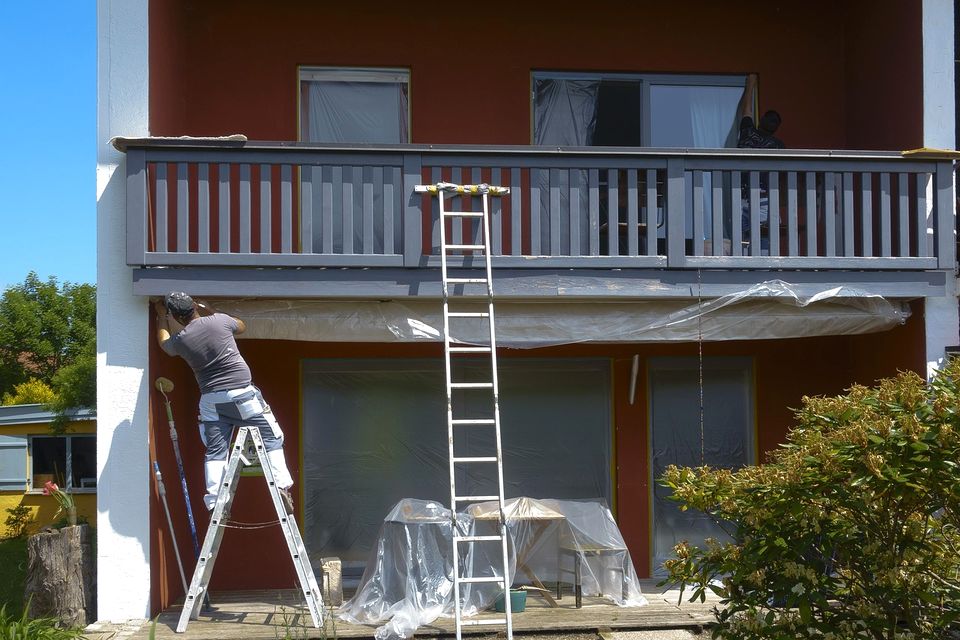 Painter on a ladder painting the siding of a house with windows masked