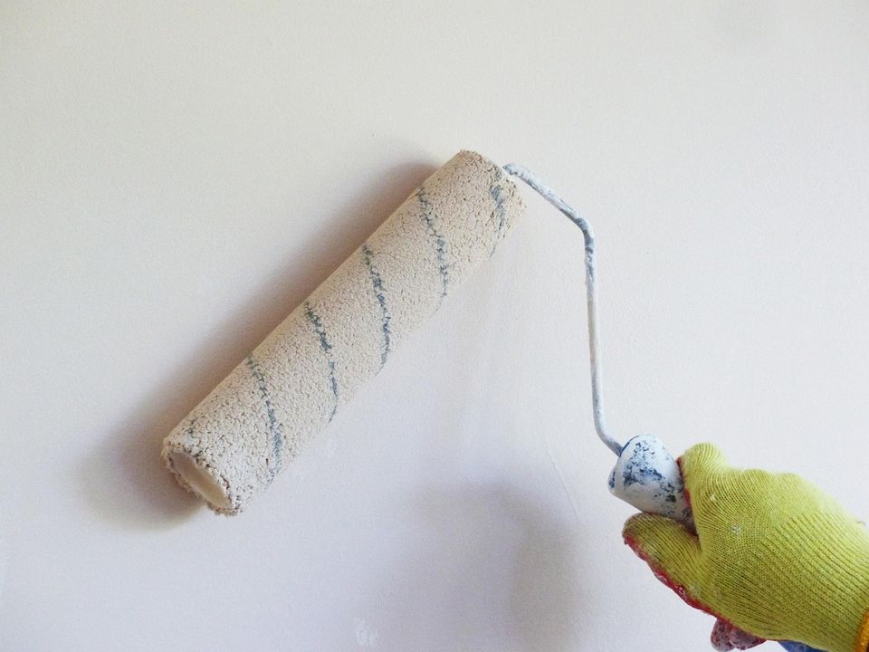 Paint roller rolling fresh white paint onto a wall