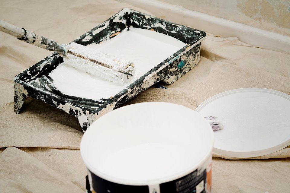 Paint tray, roller and open can of white paint on a drop cloth